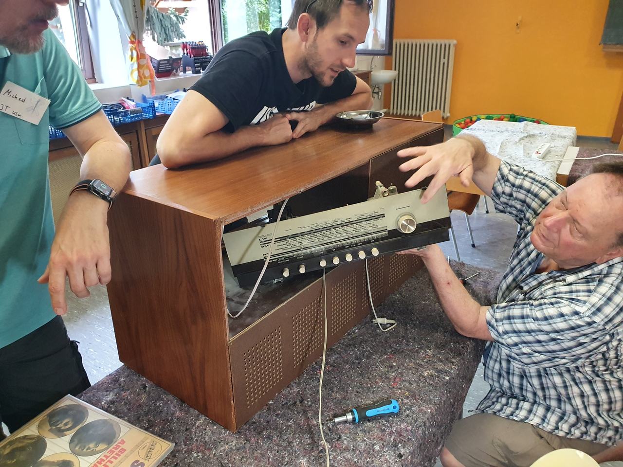 Vier Helfer stehen um ein geöffnetes Röhrenradio im Holzgehäuse und begutachten gemeinsam die Technik.